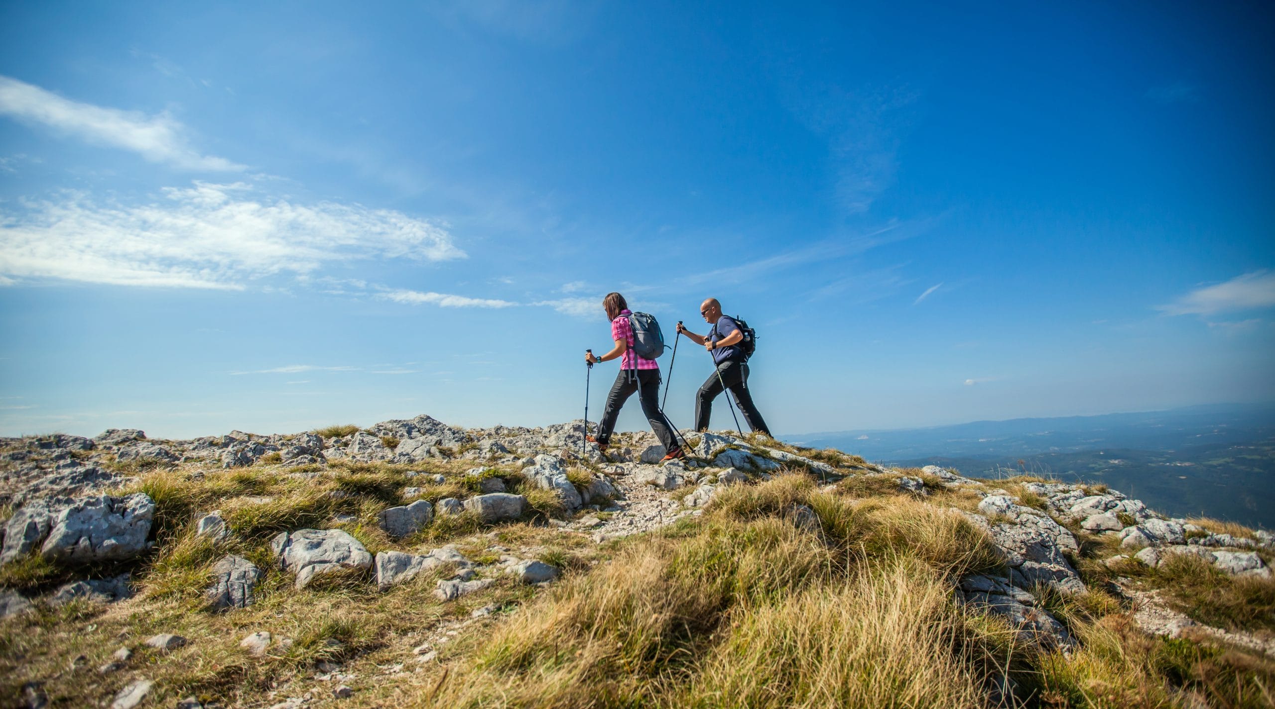 A couple hiking on Nanos Plateau in Slovenia against a blue sky