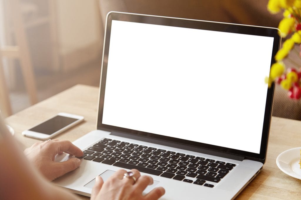 Rear view of high school girl using laptop for doing homework, browsing Internet, searching for required information, sitting at desk with mobile phone with copy space screen lying next to her