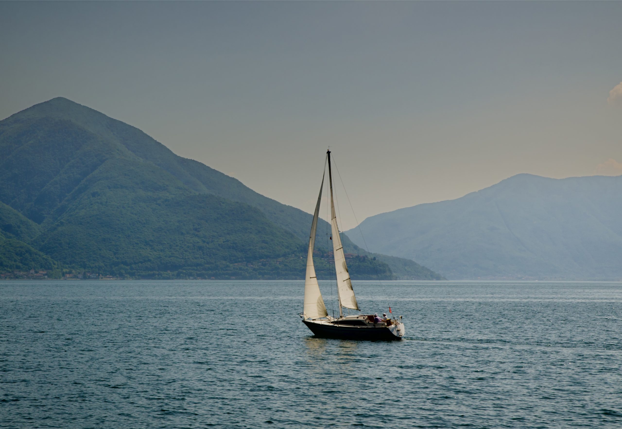 A sailing boat in the middle of the calm sea by the hills captured in Switzerland